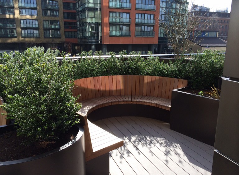 Curved wooden seating area with bushes and large planters