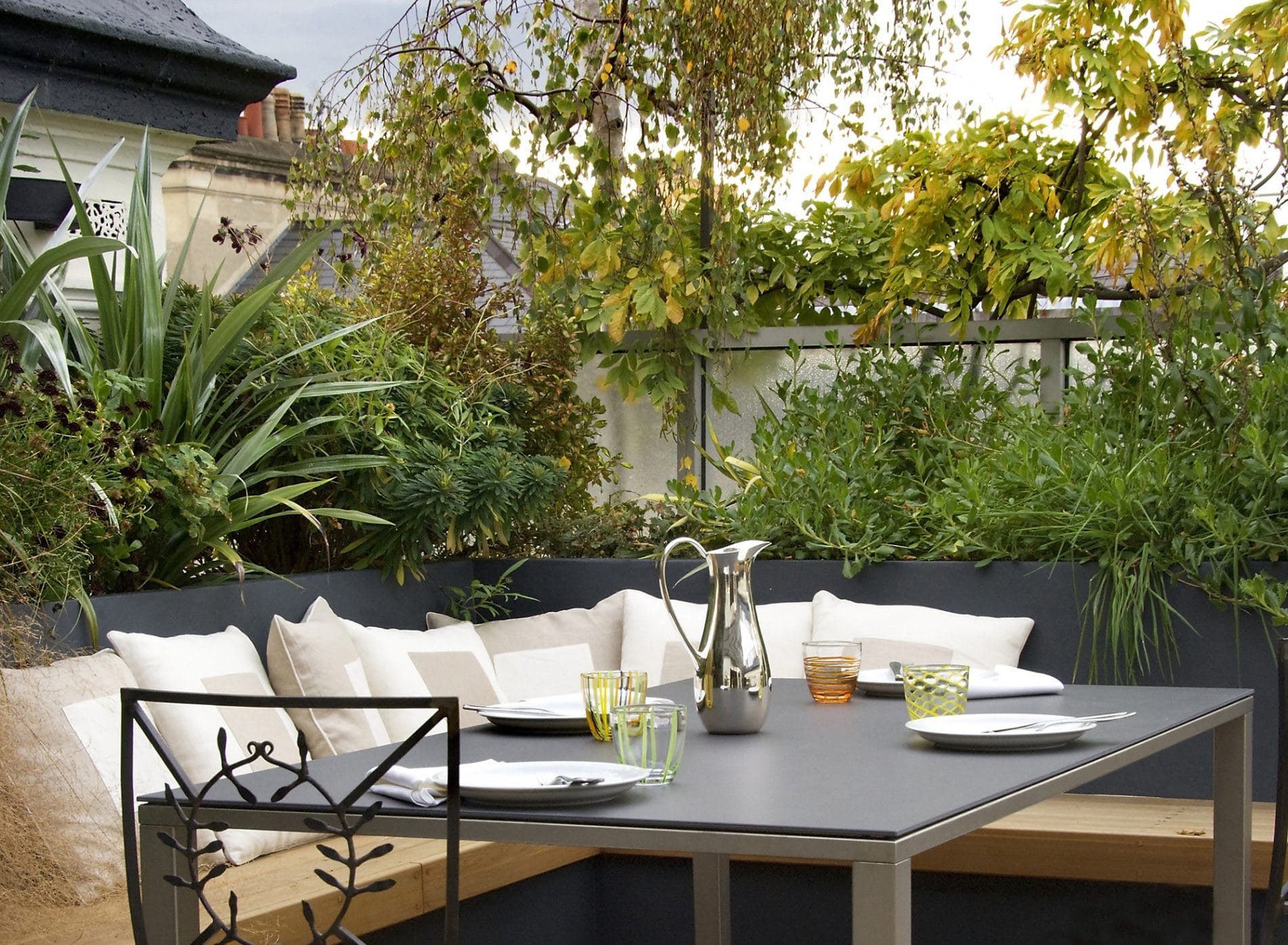 View of the outdoor dining area with comfy cushions and bright greenery surrounding