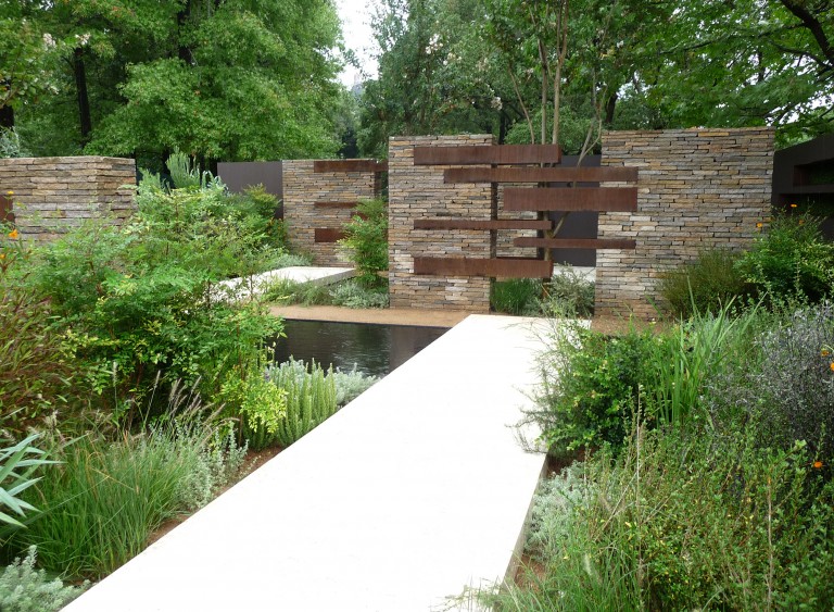 View down the path towards a tree being embraced by metal and stone