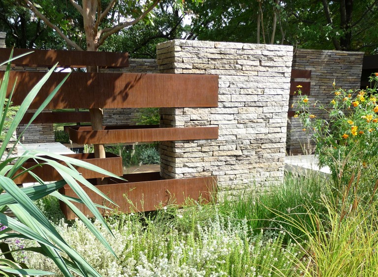 Detail of metal and stone surrounding a tree with planting around
