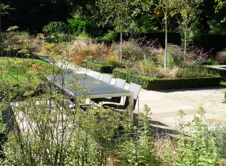 Outdoor dining area viewed through the plants in the Modern Parterre garden