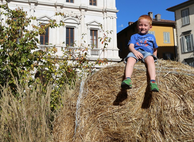 A child sits on a haybale in the piazza