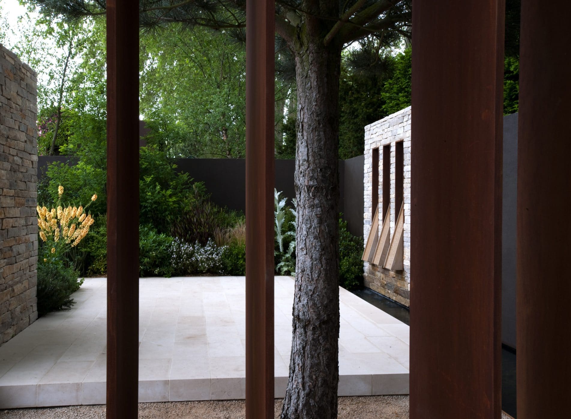 Looking through metal bars to the garden beyond with marble floors and stone walls contrasting the planting