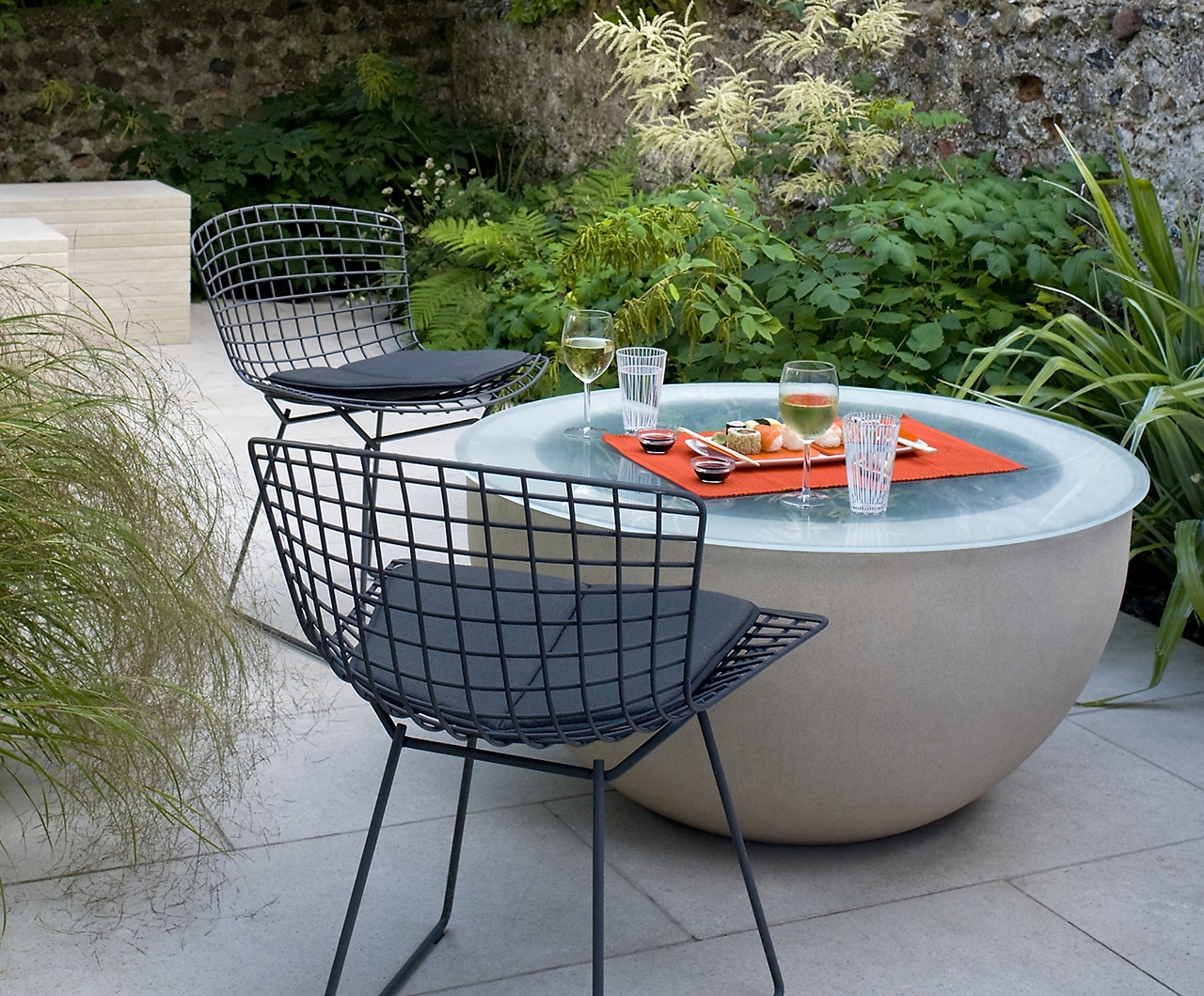 Unusual seating area with round glass table, set for a sushi meal in a small studio garden