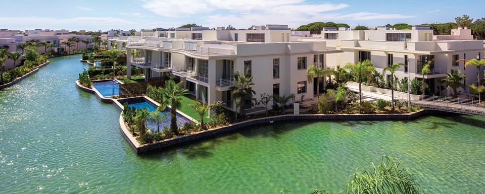 Modern Building Complex With Clear River Surrounding Featuring Palm Trees And Swimming Pools