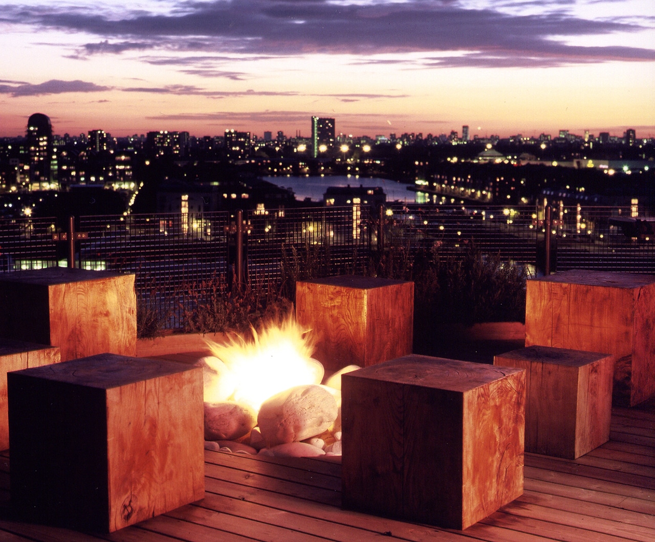 Roof garden with cube seating surrounding a firepit, looking out over London Docklands during a stunning sunset