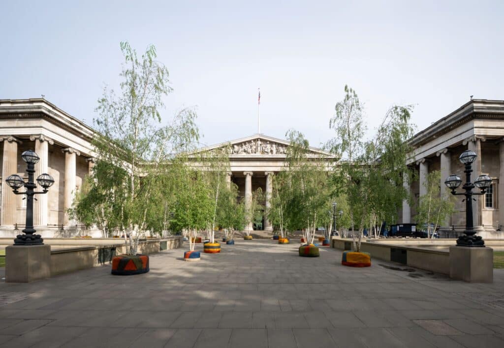 Birch trees wrapped in colourful hessian lined up in front of the British Museum